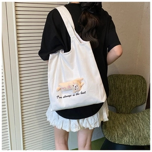 Detail of white canvas tote bag featuring a 3D plush doll and embroidered lettering