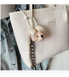 Close-up of cute plush bear charm with silk bow attached to a large white tote bag