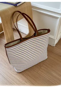 Detail of blue and white striped tote bag with brown leather handles on wooden stool