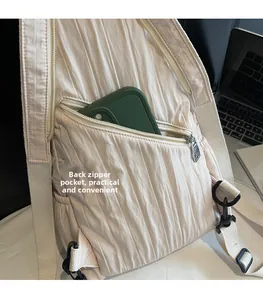 Detail of the back zipper pocket on a cream pleated crossbody bag with a green smartphone