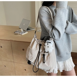 Detail view of large beige drawstring crossbody bag with plush puppy charm and front pockets
