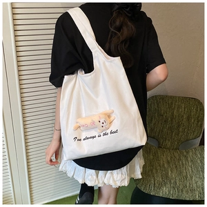 Side view of a white canvas tote bag with a pink plush charm on a female model