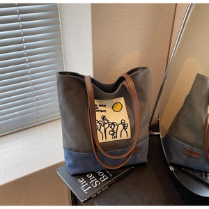 Detail of grey canvas tote with blue bottom and leather handles on a lifestyle book background