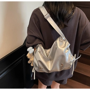 Détail du sac argenté avec papillons 3D et peluche de chien marron suspendue en décoration
