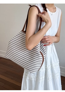 Close-up of cream canvas tote bag with black stripes and brown leather trim on a model