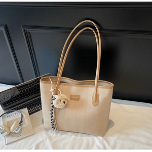 Close-up of beige tote bag with woven texture, leather handles and a cute bear charm