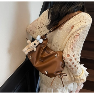 Détail d'un sac plissé marron avec papillon argenté et porte-clé chien en peluche doux