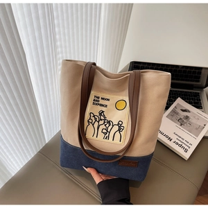 Detail view of canvas and denim patchwork tote with leather straps and embroidery text