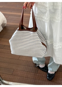 Close-up of blue striped canvas tote bag with brown leather handles and sturdy stitching