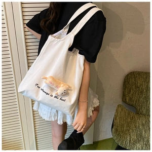 Detail of white canvas tote bag featuring a cute orange cat plush and stylish black text