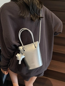 Silver metallic bucket bag with leather texture and elephant charm shown on model