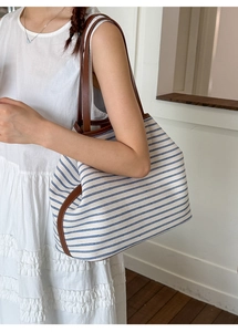 Detail of canvas tote bag with blue stripes and brown leather trim on female model
