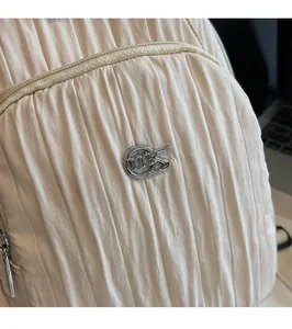 Detail of beige pleated fabric texture with silver circular metal logo and zip