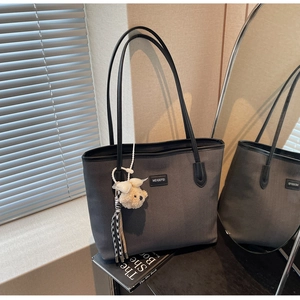 Detailed view of a grey tote bag featuring herringbone texture and a plush bear charm