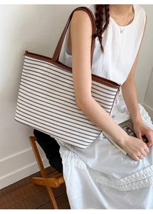 Striped canvas tote bag with brown leather handles worn by a model in a minimal setting
