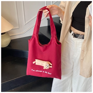Close-up of red canvas tote bag featuring a 3D plush puppy pendant and long shoulder strap