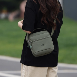 Détail du sac bandoulière en nylon vert armée montrant la sangle et le logo métallique