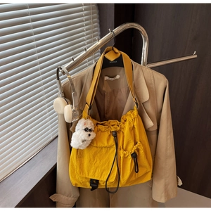 Detail of yellow drawstring shoulder bag with front buckle pocket and plush dog charm on coat