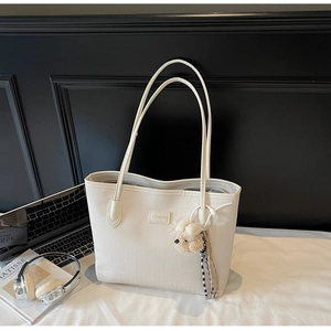 Detail of cream tote bag featuring herringbone texture, slim straps, and cute bear charm