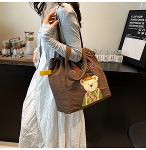 Detailed close-up of cute bear embroidery on a brown canvas tote bag with stape lettering