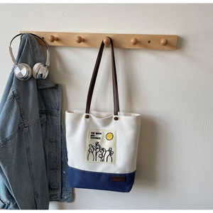 Detail of color-block canvas tote bag with artistic print hanging on a wooden hook