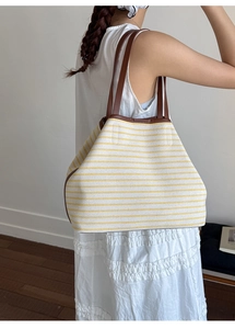 Model wearing a large striped canvas tote bag with brown leather straps for commuting