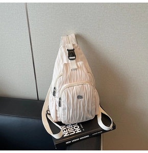 Close-up of beige pleated fabric crossbody bag with metal logo and quick release buckle