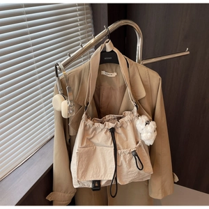 Detail of light beige drawstring bucket bag with flap pockets and plush pendant