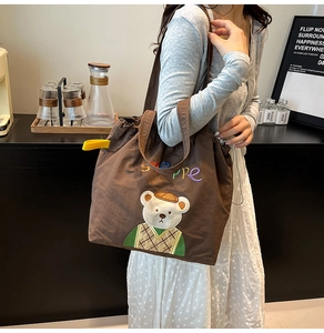 Close-up of brown canvas tote bag featuring cute teddy bear embroidery and steppe lettering