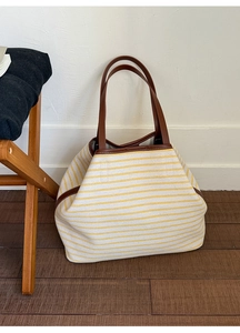 Detail of striped canvas tote bag with brown leather handles on wooden floor