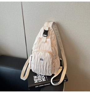 Detail of beige pleated crossbody bag featuring a front zipper and adjustable shoulder strap