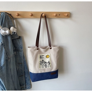 Detail of canvas tote bag hanging on wooden rack with leather straps and contrast trim