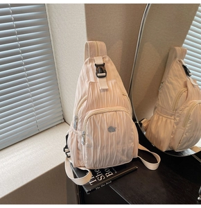 Detail view of beige pleated crossbody bag featuring metal logo and layered zipper compartments