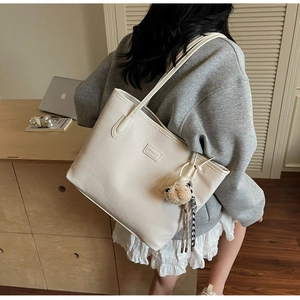 Detail of cream tote bag featuring V-shaped woven texture and cute plush bear charm