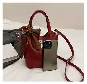 Secchiello in pelle rossa con fiocco in seta accanto a uno smartphone per confronto taglia