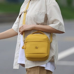 Détail du sac bandoulière en nylon jaune résistant à l'eau avec logo et poche zippée
