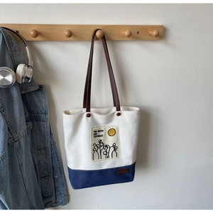 Detail of canvas tote with embroidery and leather straps against a white wall