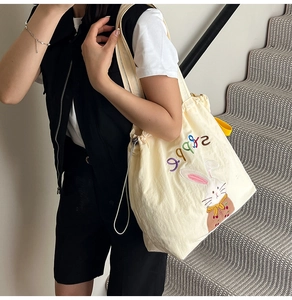 Detail of cream canvas tote bag featuring cute rabbit embroidery and colorful happy text