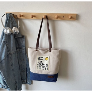 Detail of canvas tote bag hanging on wooden hook with blue jacket and headphones