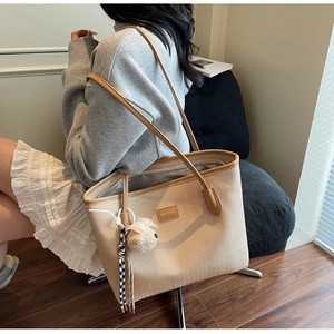Detail of beige herringbone tote bag with brown leather straps and plush bear charm