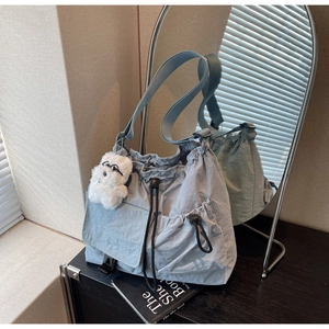 Detail of light blue nylon crossbody bag with drawstring closure and plush dog charm