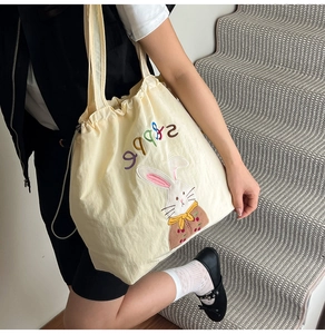 Close-up of beige canvas tote bag featuring cute cartoon rabbit embroidery and drawstring