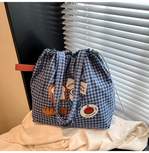 Detail of blue plaid canvas tote with embroidery and drawstring closure on white fabric