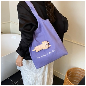 Detail of purple canvas tote bag with plush animal toy and white embroidered text