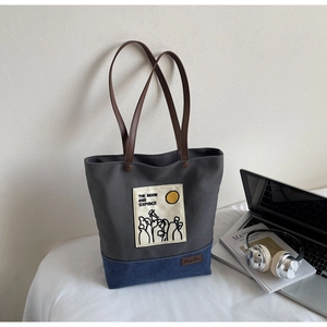 Detail of grey and navy canvas tote bag featuring brown leather straps and artistic embroidery
