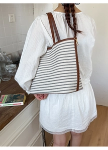Detail of striped canvas tote with brown leather handles and golden metal buckles