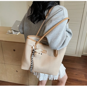 Close-up of beige herringbone tote bag with brown leather handles and puppy charm