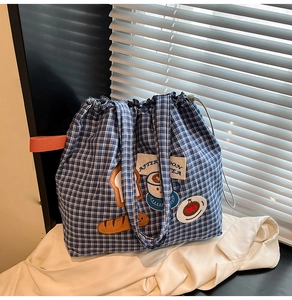 Detail view of blue plaid canvas tote bag featuring embroidered food patches and drawstring
