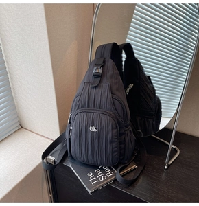Detail of black pleated fabric crossbody bag showing zipper pocket and metal logo detail