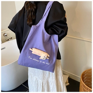 Detail of purple canvas tote bag featuring a cute plush doll ornament and white lettering